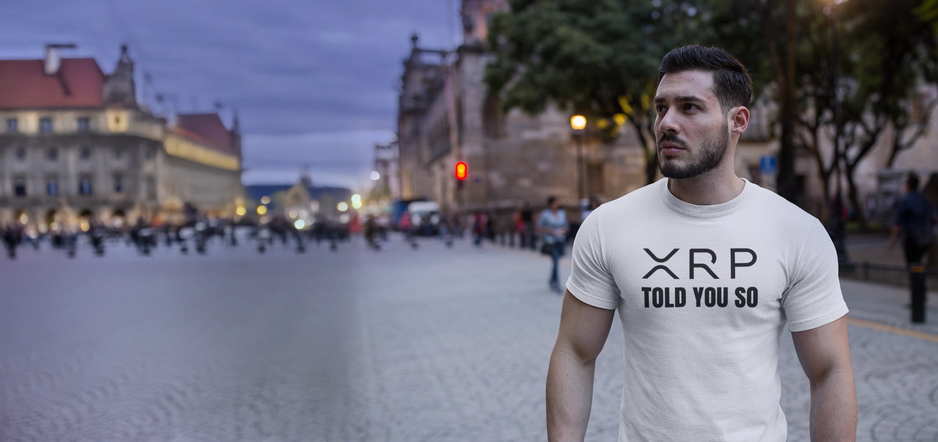 Man wearing a t-shirt with 'XRP TOLD YOU SO' on a city street at dusk.